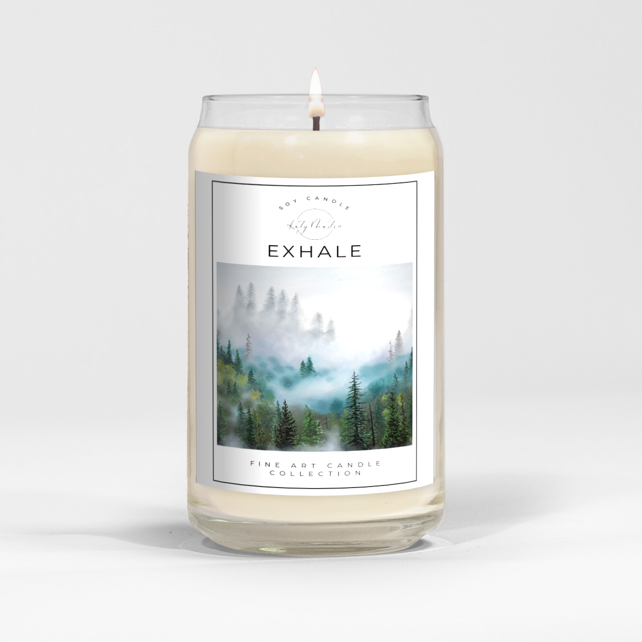 close up of burning white wax candle in a clear glass vessel with fine art landscape painting by Manitoba Artist Katy Martin on label