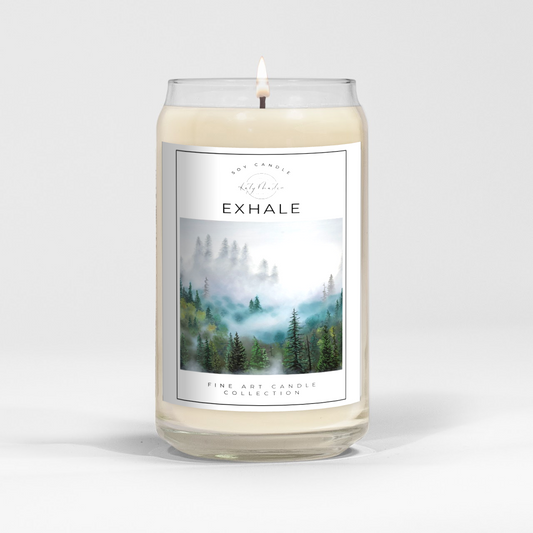 close up of burning white wax candle in a clear glass vessel with fine art landscape painting by Manitoba Artist Katy Martin on label