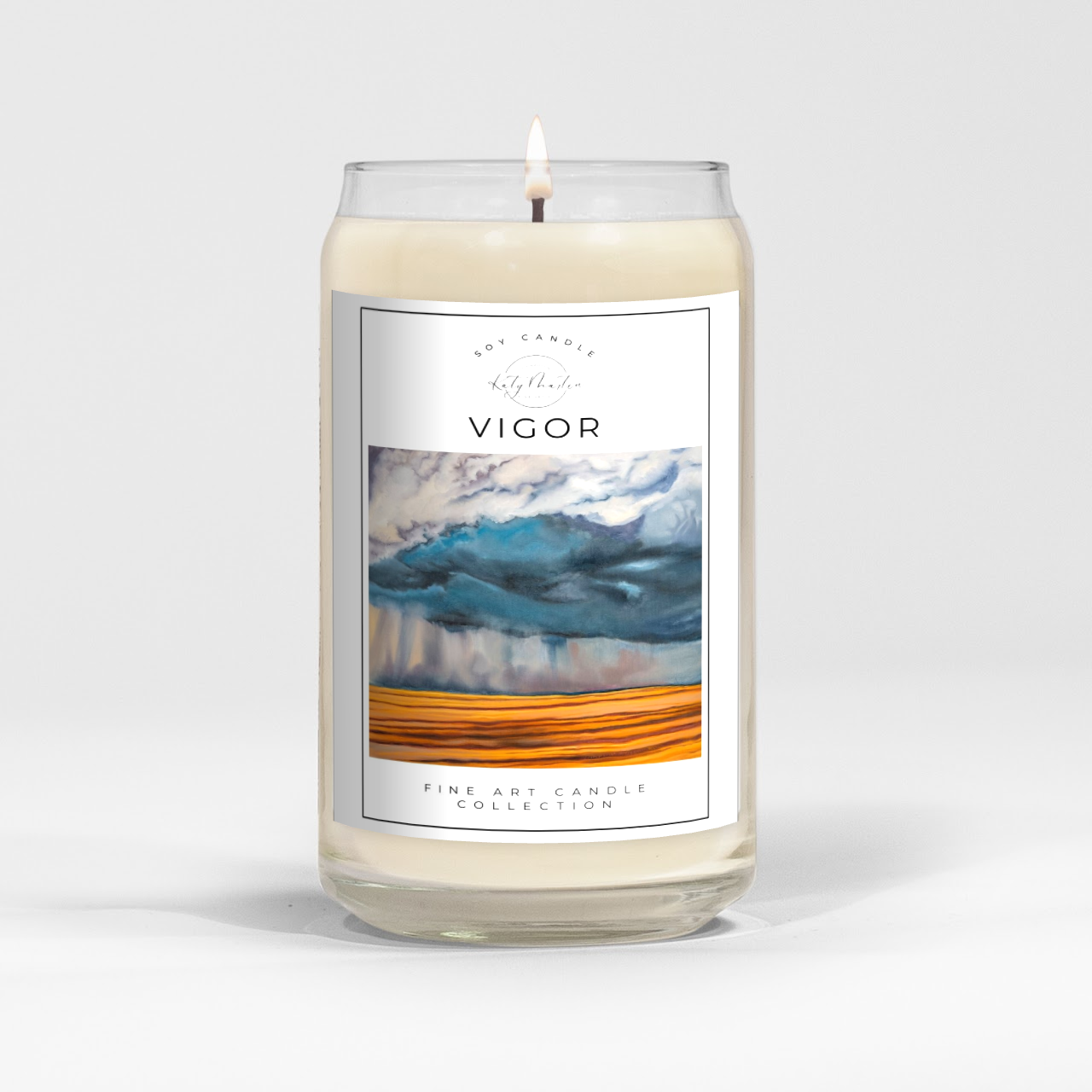 close up of burning white wax candle in a clear glass vessel with fine art landscape painting of a prairie storm by Manitoba Artist Katy Martin on label
