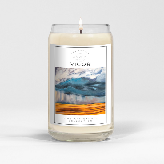 close up of burning white wax candle in a clear glass vessel with fine art landscape painting of a prairie storm by Manitoba Artist Katy Martin on label