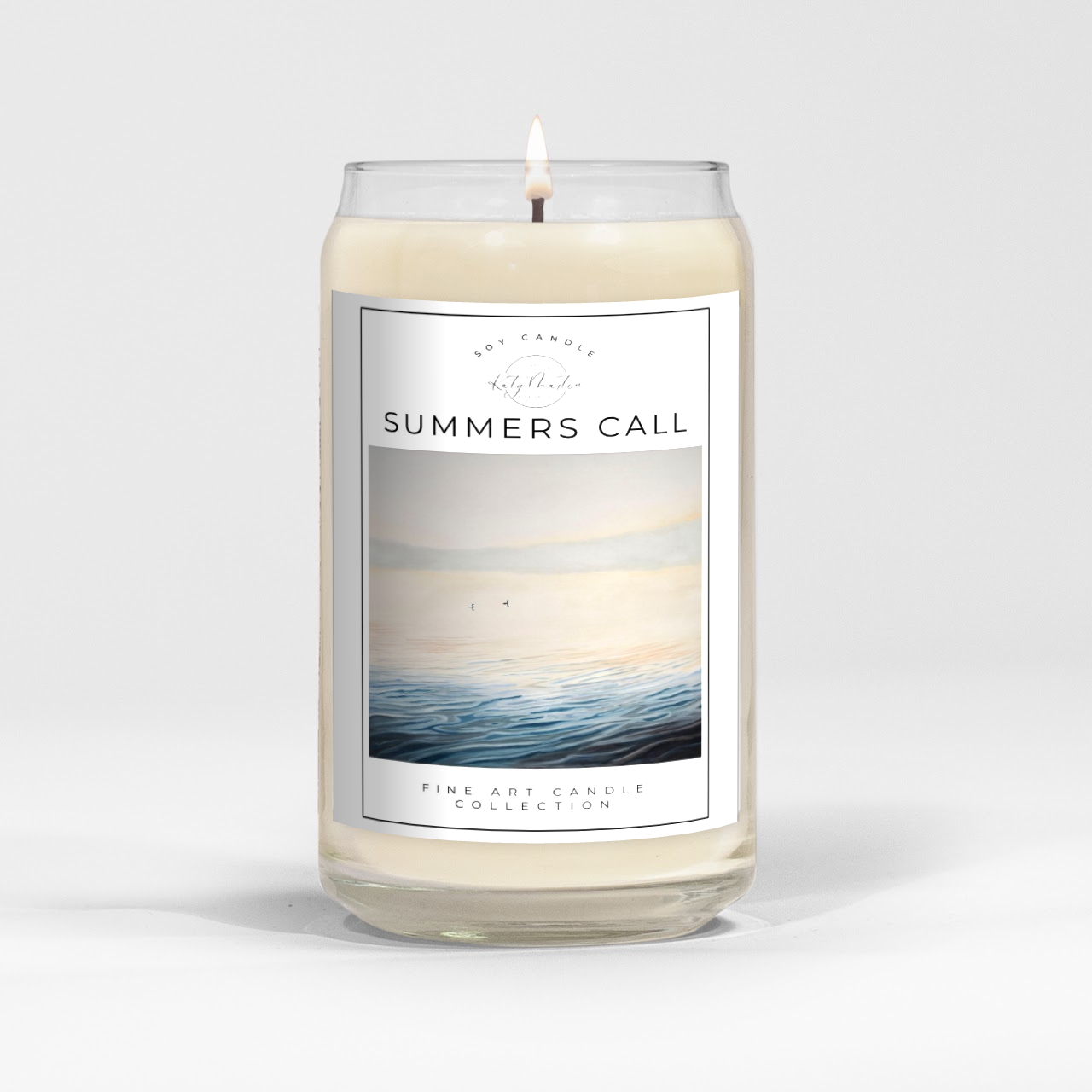 close up of burning white wax candle in a clear glass vessel with fine art landscape painting of loons on a misty lake by Manitoba Artist Katy Martin on label