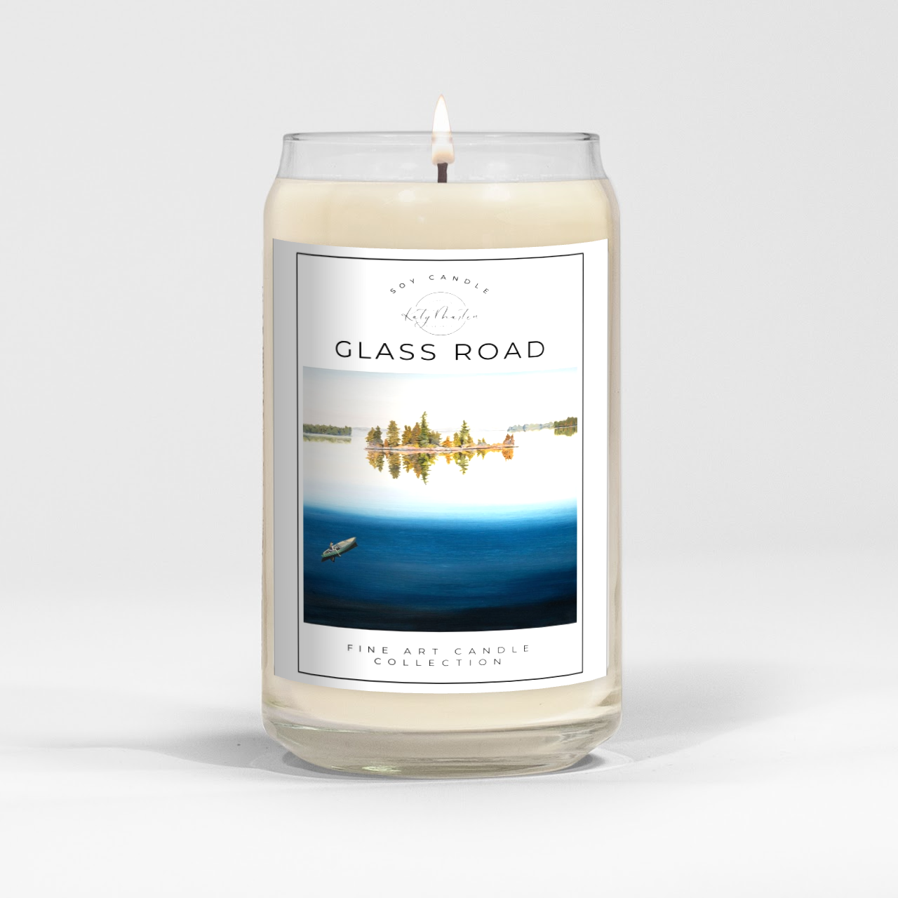 close up of burning white wax candle in a clear glass vessel with fine art landscape painting by Manitoba Artist Katy Martin on label