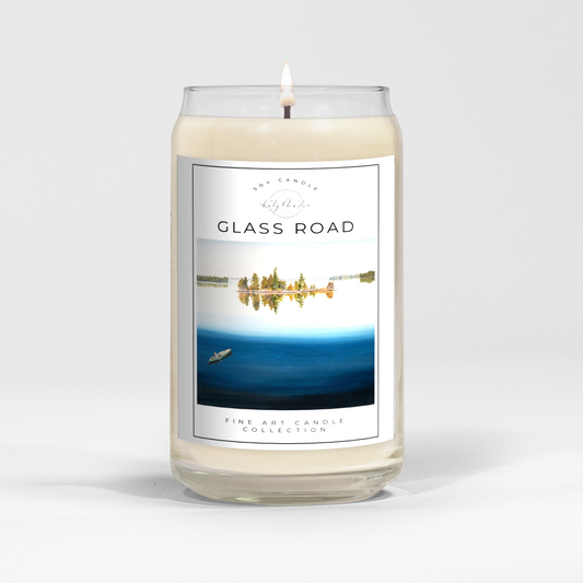 close up of burning white wax candle in a clear glass vessel with fine art landscape painting by Manitoba Artist Katy Martin on label