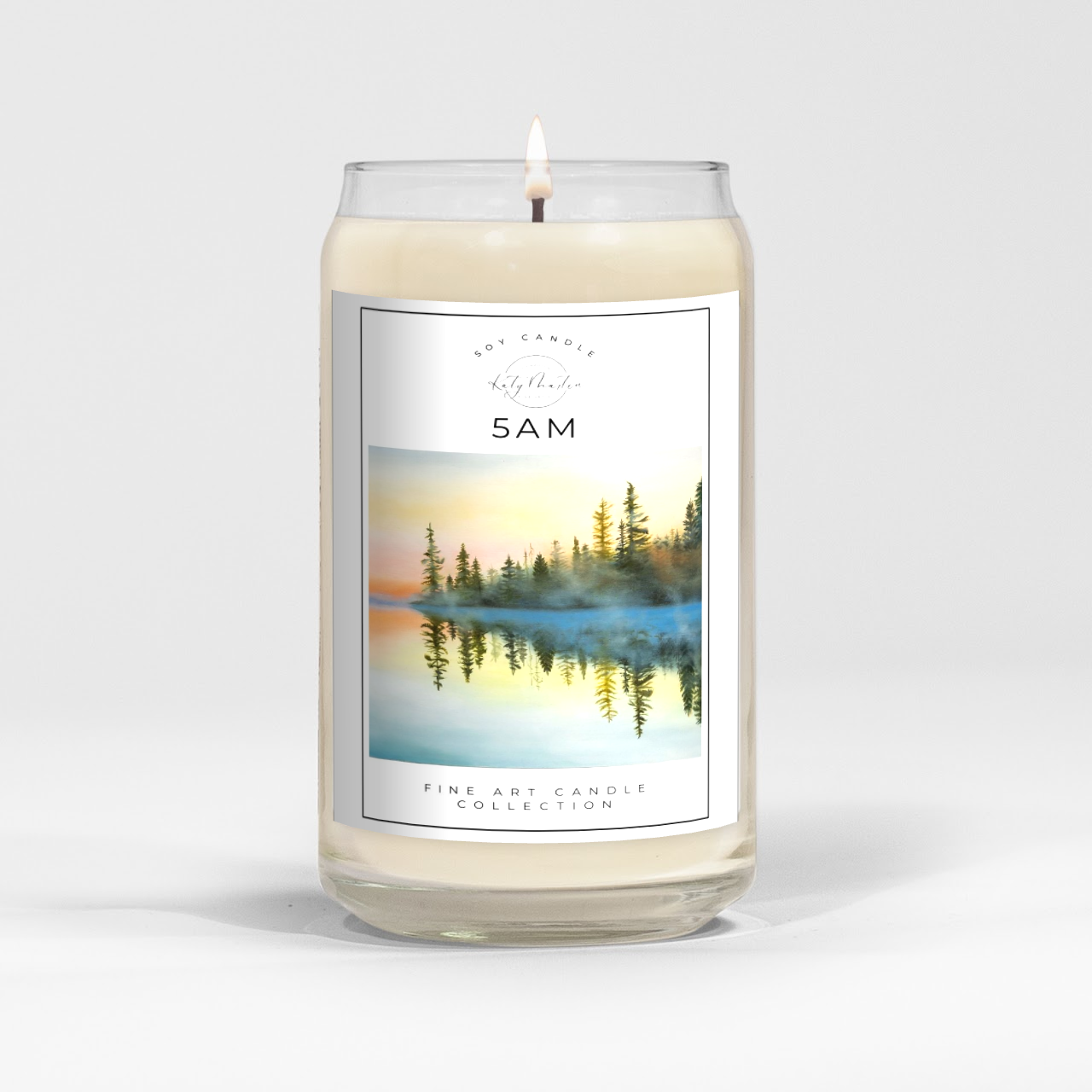 close up of burning white wax candle in a clear glass vessel with fine art landscape painting by Manitoba Artist Katy Martin on label