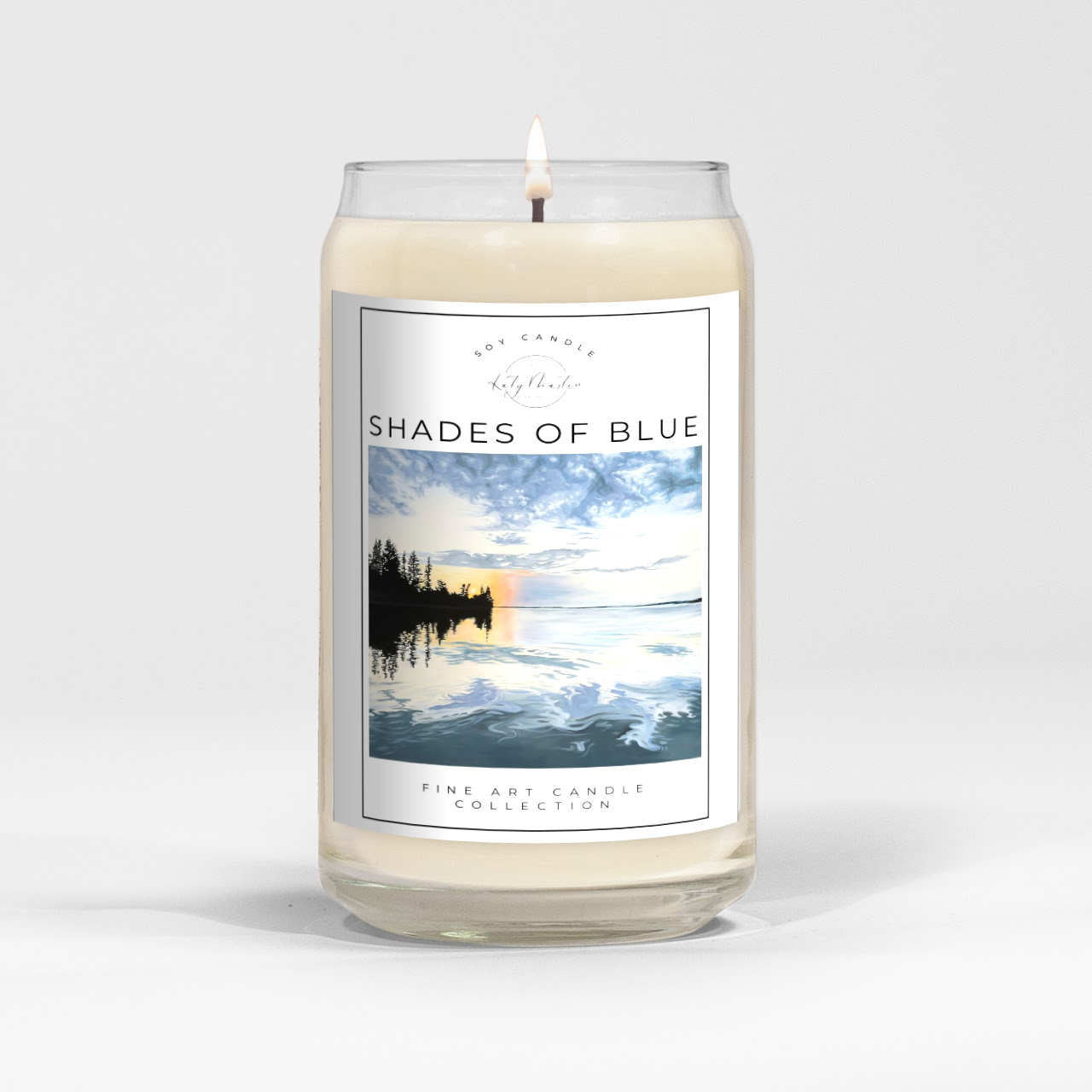close up of burning white wax candle in a clear glass vessel with fine art landscape painting by Manitoba Artist Katy Martin on label