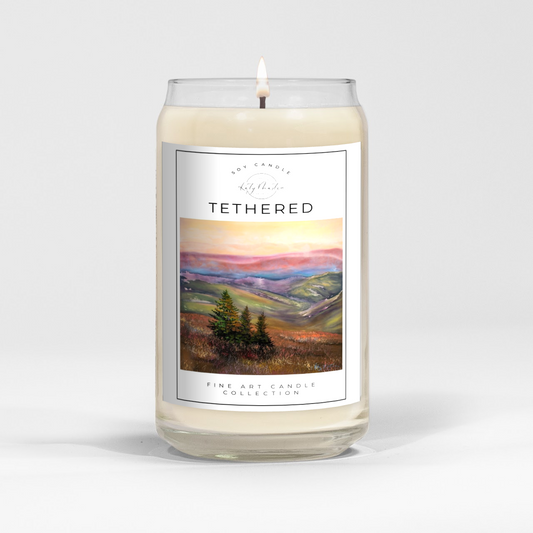close up of burning white wax candle in a clear glass vessel with fine art landscape painting by Manitoba Artist Katy Martin on label
