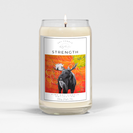 close up of burning white wax candle in a clear glass vessel with fine art wildlife painting of a moose by Manitoba Artist Katy Martin on label