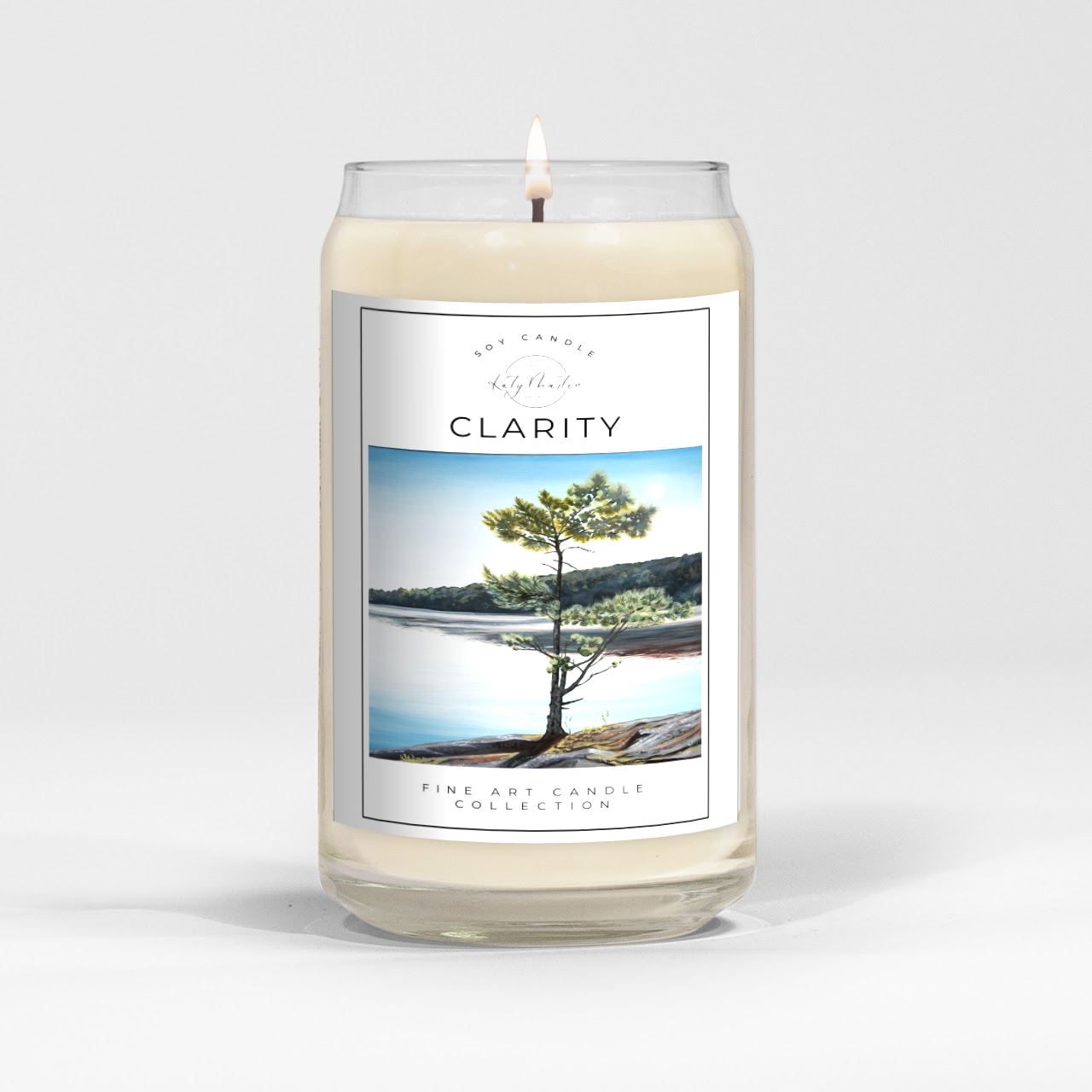 close up of burning white wax candle in a clear glass vessel with fine art landscape painting by Manitoba Artist Katy Martin on label