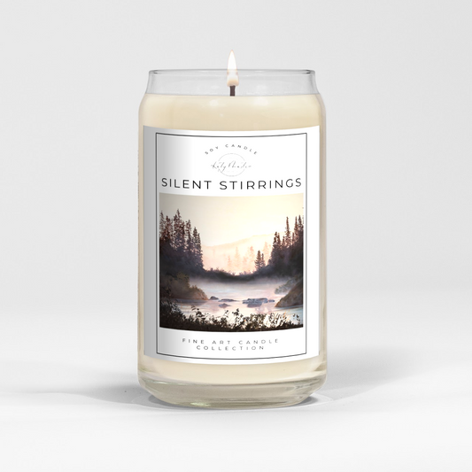 close up of burning white wax candle in a clear glass vessel with fine art landscape painting of a misty lake by Manitoba Artist Katy Martin on label