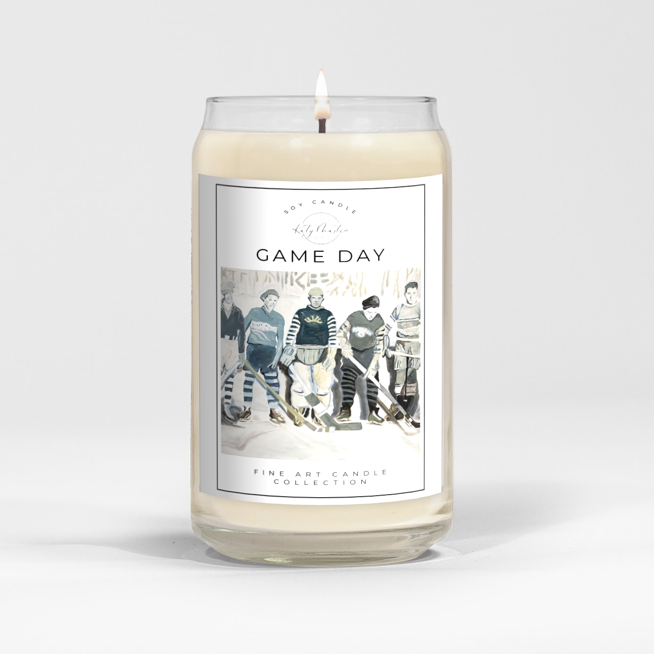 close up of burning white wax candle in a clear glass vessel with fine art retro hockey painting by Manitoba Artist Katy Martin on label