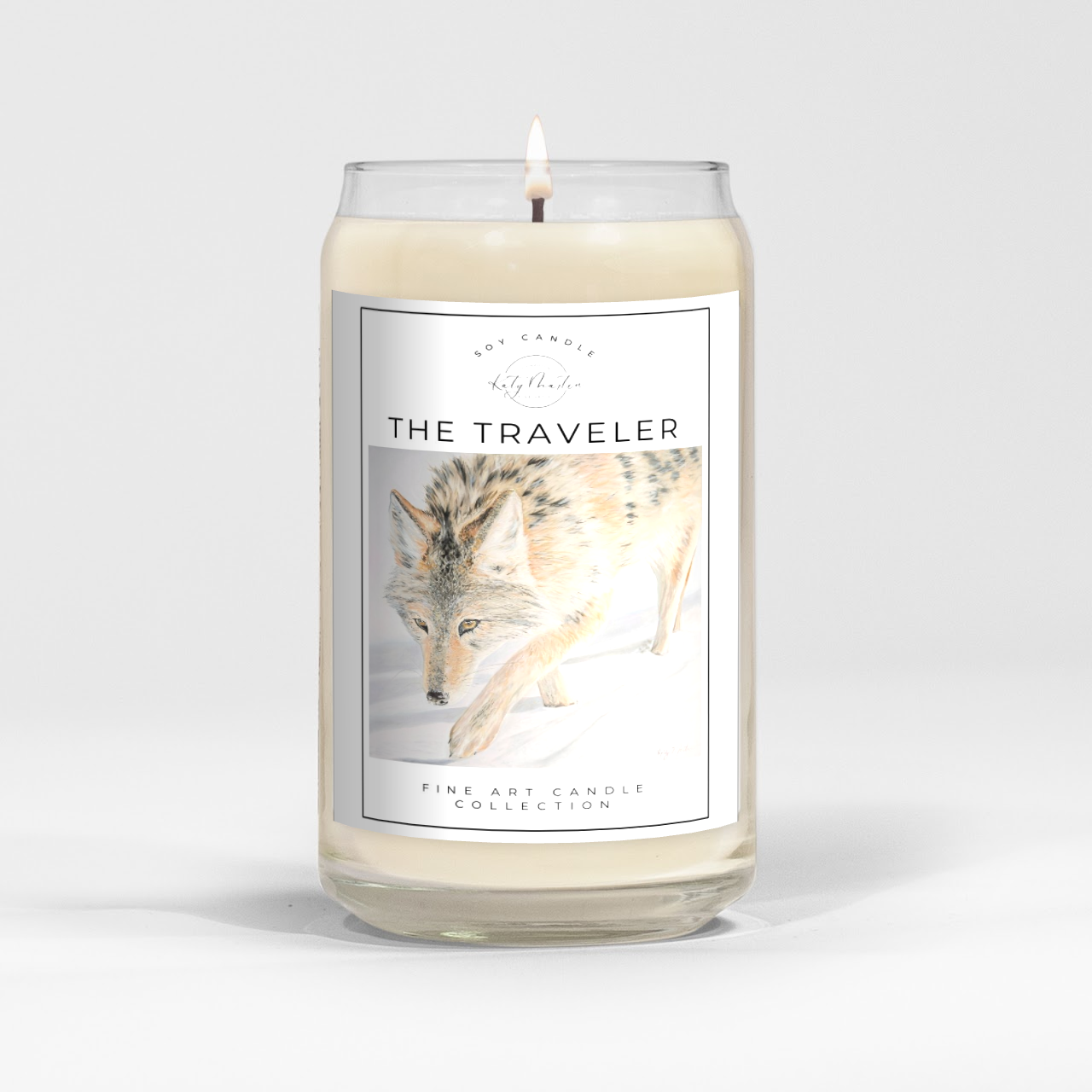 close up of burning white wax candle in a clear glass vessel with fine art wildlife painting of a wolf by Manitoba Artist Katy Martin on label