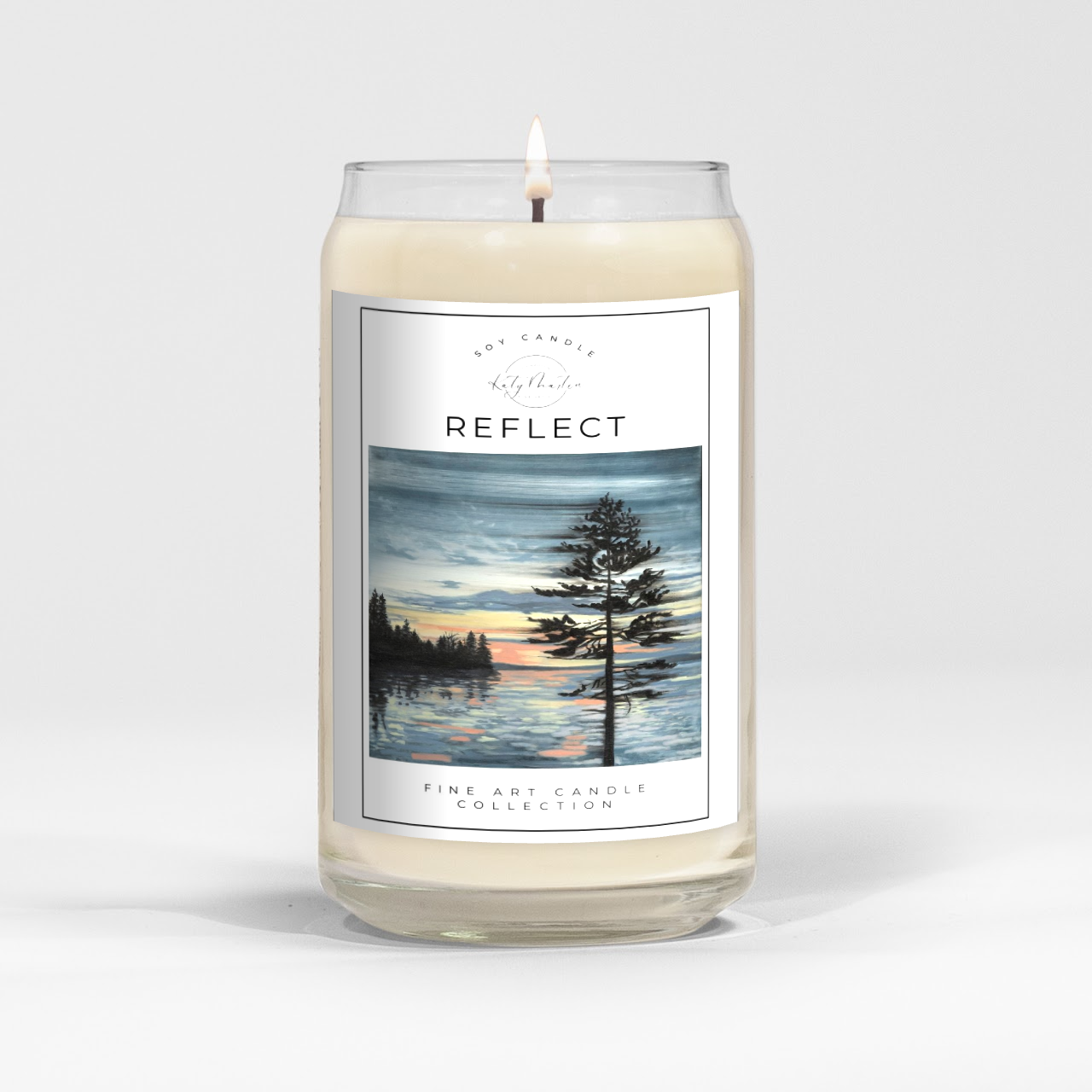 close up of burning white wax candle in a clear glass vessel with fine art landscape painting by Manitoba Artist Katy Martin on label