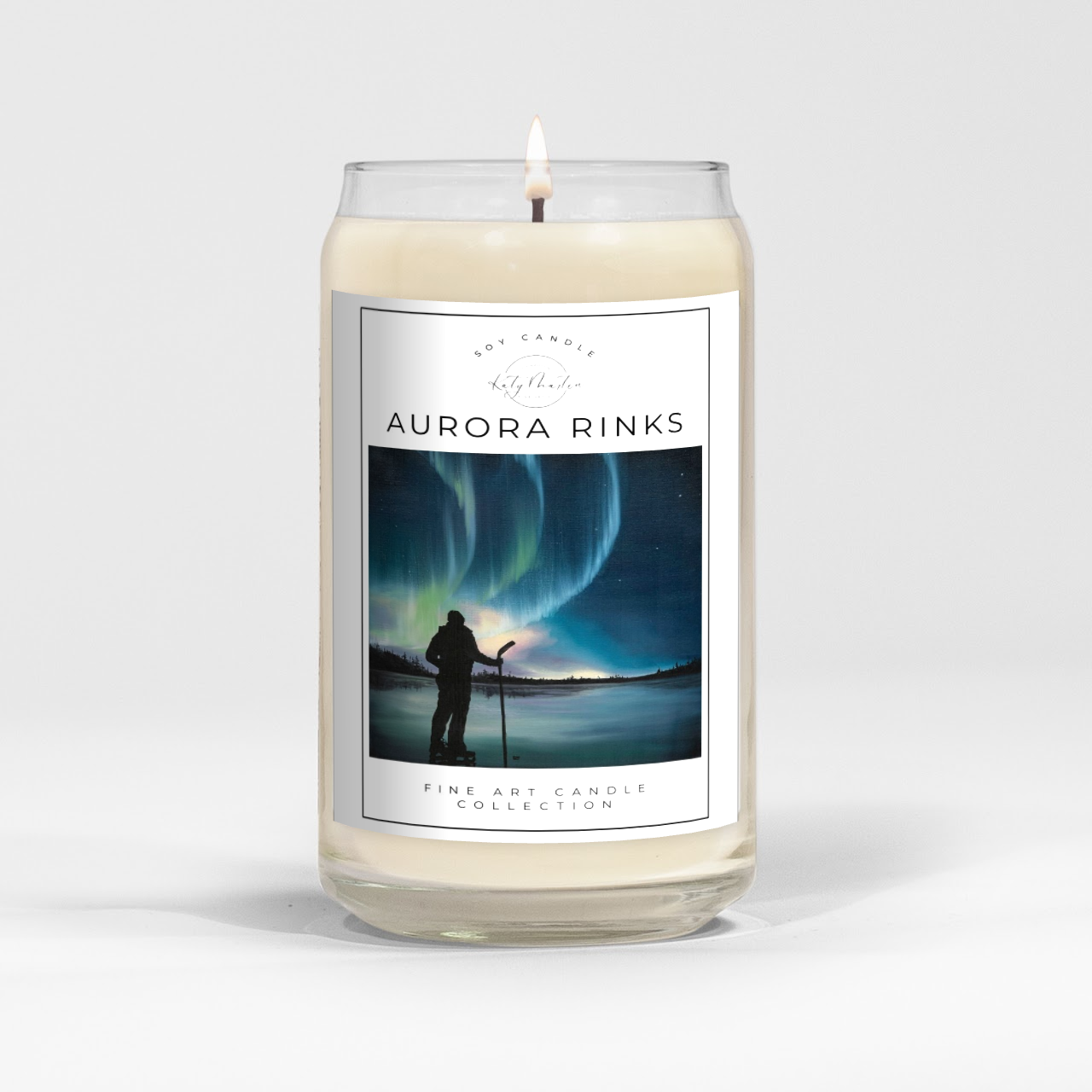 close up of burning white wax candle in a clear glass vessel with fine art landscape painting by Manitoba Artist Katy Martin on label