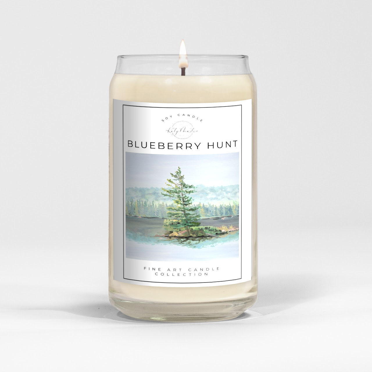 close up of burning white wax candle in a clear glass vessel with fine art landscape painting by Manitoba Artist Katy Martin on label