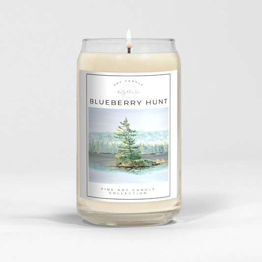 close up of burning white wax candle in a clear glass vessel with fine art landscape painting by Manitoba Artist Katy Martin on label