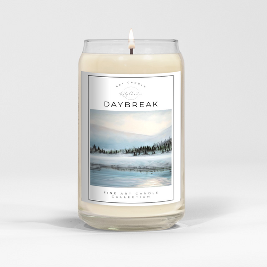 close up of burning white wax candle in a clear glass vessel with fine art landscape painting by Manitoba Artist Katy Martin on label