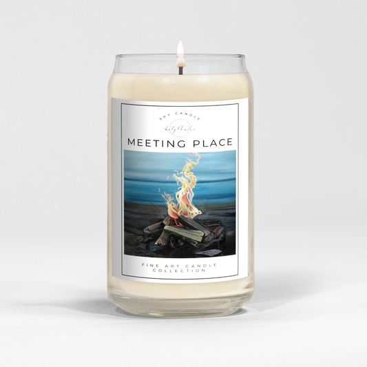 close up of burning white wax candle in a clear glass vessel with fine art landscape painting of a lakeside fire by Manitoba Artist Katy Martin on label 