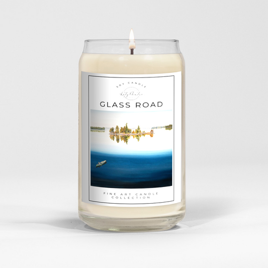 close up of burning white wax candle in a clear glass vessel with fine art landscape painting by Manitoba Artist Katy Martin on label 